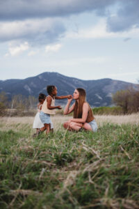 mom and her daughters smelling flowers in a field
