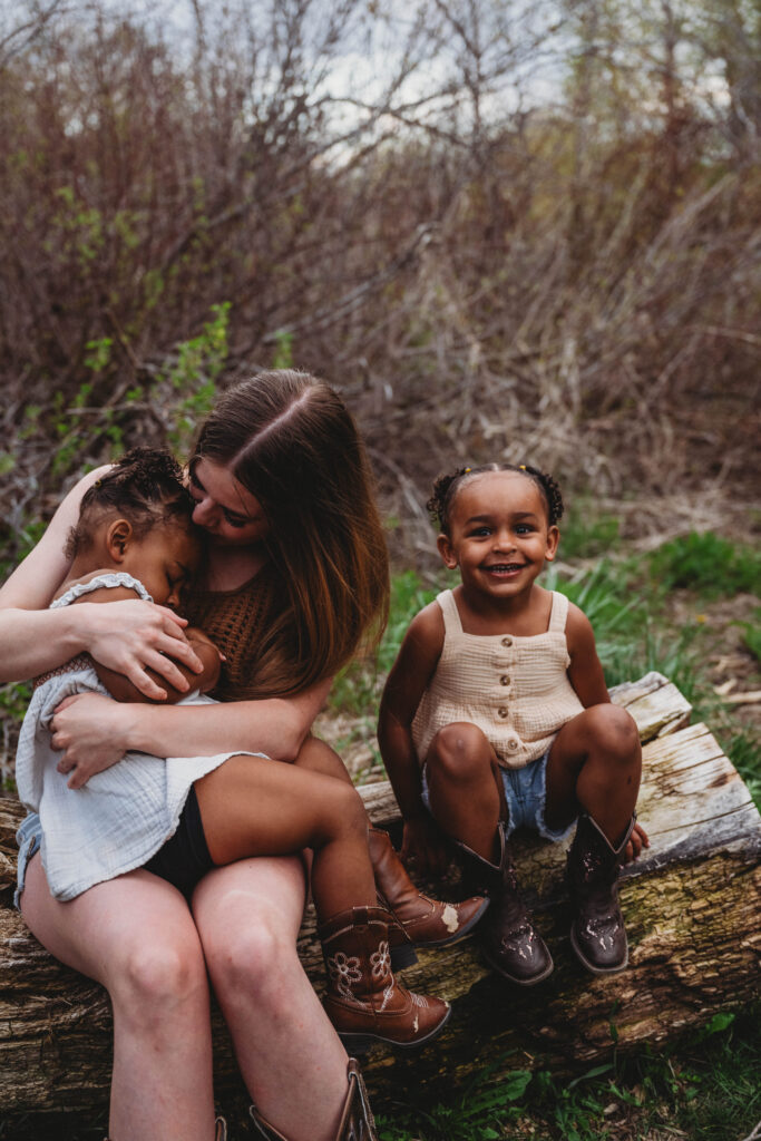 mom and girls sitting on a log in the woods