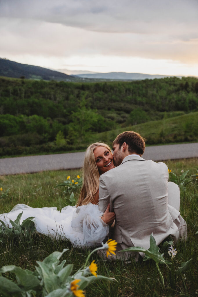 a newly married couple taking a minute to sit in the grass and watch the sunset